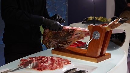 Image showing Sliced dried chamon prosciutto. A man cuts a jamon, a warm toned