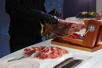 Image showing Sliced dried chamon prosciutto. A man cuts a jamon, a warm toned image. Selective focus point.