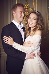 Image showing Wedding couple indoors is hugging each other. Beautiful model girl in white dress. Man in suit. Beauty bride with groom. Female and male portrait. Woman with lace veil. Cute lady and handsome guy