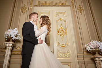 Image showing Wedding couple indoors is hugging each other. Beautiful model girl in white dress. Man in suit. Beauty bride with groom. Female and male portrait. Woman with lace veil. Cute lady and handsome guy
