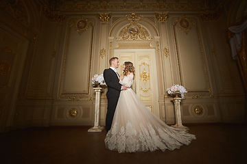 Image showing Charming wedding couple in interior in Baroque style is hugging each other on great royal palace