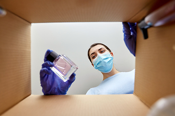 Image showing woman in mask unpacking parcel box with cosmetics