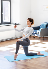 Image showing young woman with smartphone doing yoga at home