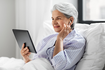 Image showing senior woman with tablet pc and earphones in bed