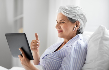 Image showing old woman with tablet pc having video call in bed