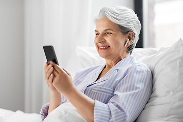 Image showing senior woman with smartphone and earphones in bed