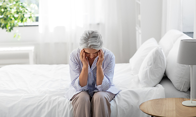 Image showing senior woman with headache sitting on bed at home