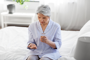 Image showing senior woman with pill and water sitting on bed