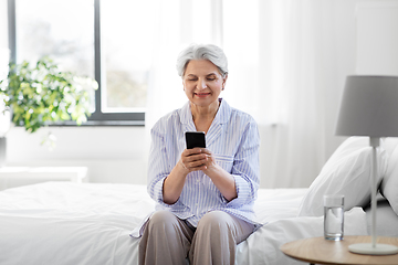 Image showing happy senior woman with smartphone on bed at home