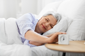 Image showing happy senior woman with alarm clock in bed at home