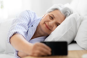 Image showing happy senior woman with smartphone in bed at home