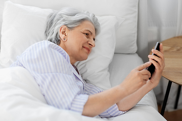 Image showing happy senior woman with smartphone in bed at home