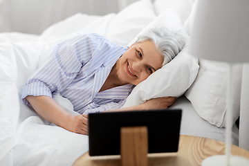 Image showing happy senior woman with tablet pc in bed at home