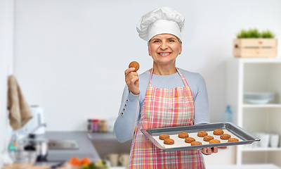 Image showing senior woman in toque with cookies on baking pan