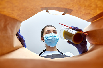 Image showing saleswoman in gloves and mask packing food in bag