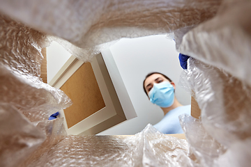 Image showing woman in mask opening parcel box with photo frame