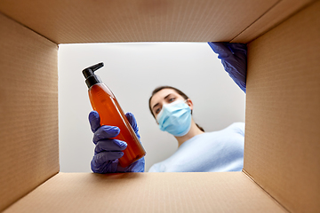 Image showing woman in mask unpacking parcel box with cosmetics