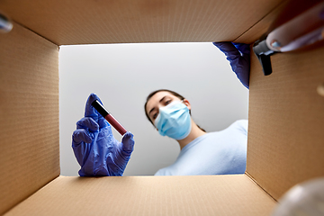 Image showing woman in mask unpacking parcel box with cosmetics