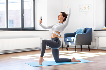 Image showing young woman with smartphone doing yoga at home