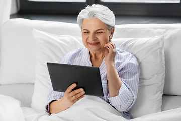 Image showing senior woman with tablet pc and earphones in bed