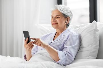 Image showing senior woman with smartphone and earphones in bed