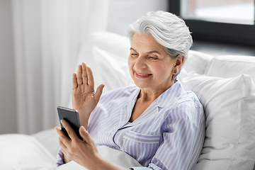 Image showing senior woman with phone having video call in bed