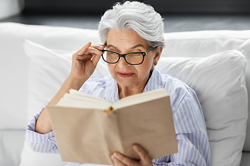 Image showing old woman in glasses reading book in bed at home