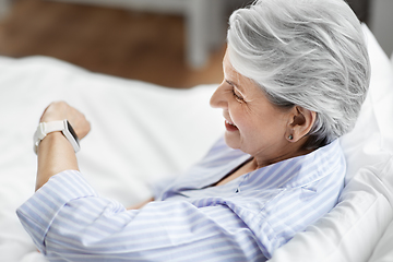 Image showing happy senior woman sitting in bed at home bedroom