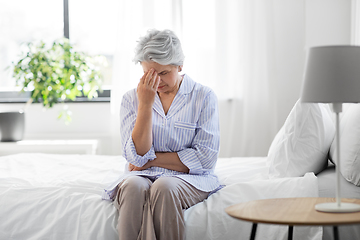 Image showing senior woman with headache sitting on bed at home