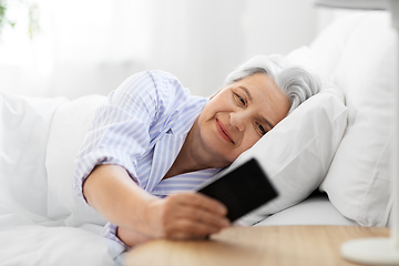 Image showing happy senior woman with smartphone in bed at home