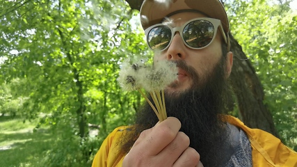 Image showing Portrait of a beard man blowing on the ripened dandelion. Slow motion video.