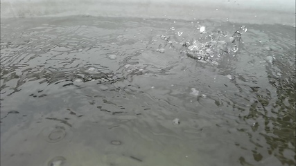 Image showing Rain water drops falling into big puddle on asphalt, flooding the street. Road floods due to the heavy rain in wet season. Raindrops falling down onto submerged road.