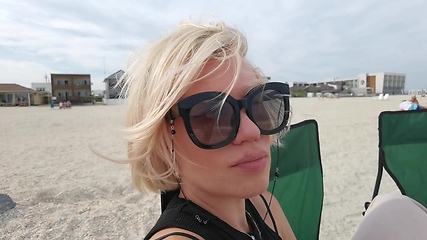 Image showing Slow motion portrait face of beautiful young woman with short blonde hair looking at camera sitting on sea beach
