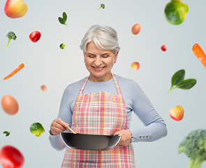 Image showing smiling senior woman in apron with frying pan