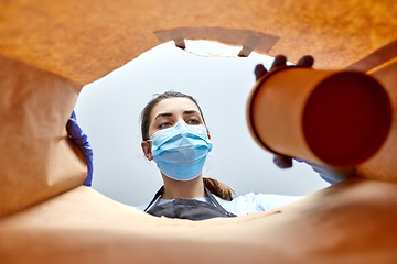 Image showing saleswoman in gloves and mask packing food in bag