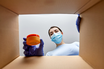 Image showing woman in mask unpacking parcel box with cosmetics