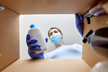 Image showing woman in mask unpacking parcel box with cosmetics