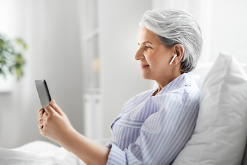 Image showing senior woman with tablet pc and earphones in bed