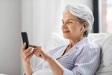 Image showing senior woman with smartphone and earphones in bed