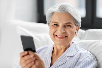 Image showing senior woman with smartphone and earphones in bed