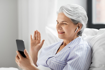 Image showing senior woman with phone having video call in bed