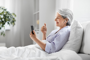 Image showing senior woman with phone having video call in bed