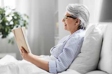 Image showing old woman in glasses reading book in bed at home