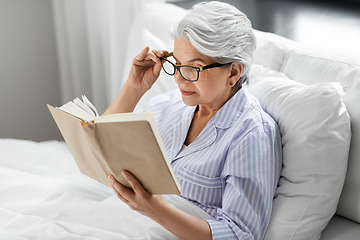 Image showing old woman in glasses reading book in bed at home