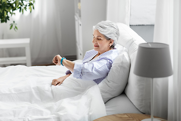 Image showing happy old woman with health tracker sitting in bed