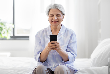 Image showing happy senior woman with smartphone on bed at home