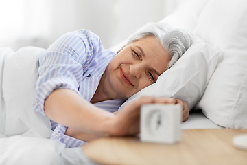 Image showing happy senior woman with alarm clock in bed at home