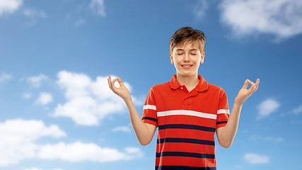 Image showing happy smiling meditating boy over blue sky