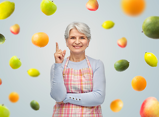 Image showing smiling senior woman in apron pointing finger up