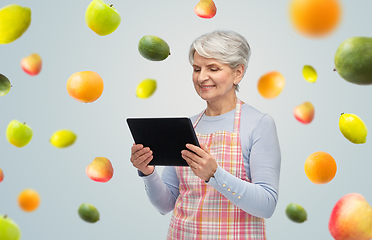 Image showing smiling senior woman in apron with tablet computer